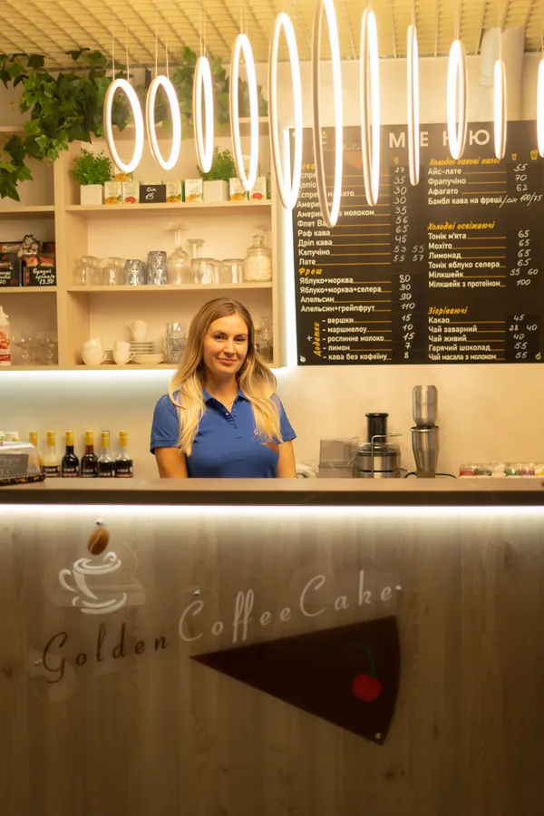 Власниця кав'ярні за стійкою з логотипом Golden CoffeeCake